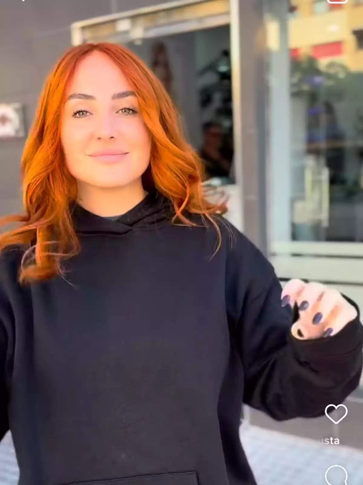Rocío Flores con cabello rojo y suelto lleva una sudadera negra mientras sonríe frente a un edificio. Rocío Flores con cabello rojo y suelto lleva una sudadera negra mientras sonríe frente a un edificio.