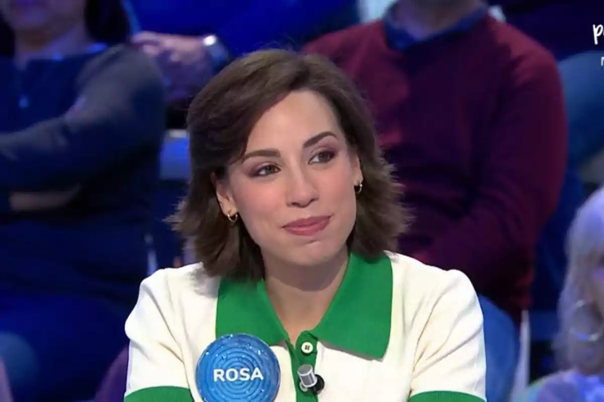 Rosa con cabello castaño y una expresión sonriente está sentada en un estudio de televisión con un público de fondo. Rosa con cabello castaño y una expresión sonriente está sentada en un estudio de televisión con un público de fondo.