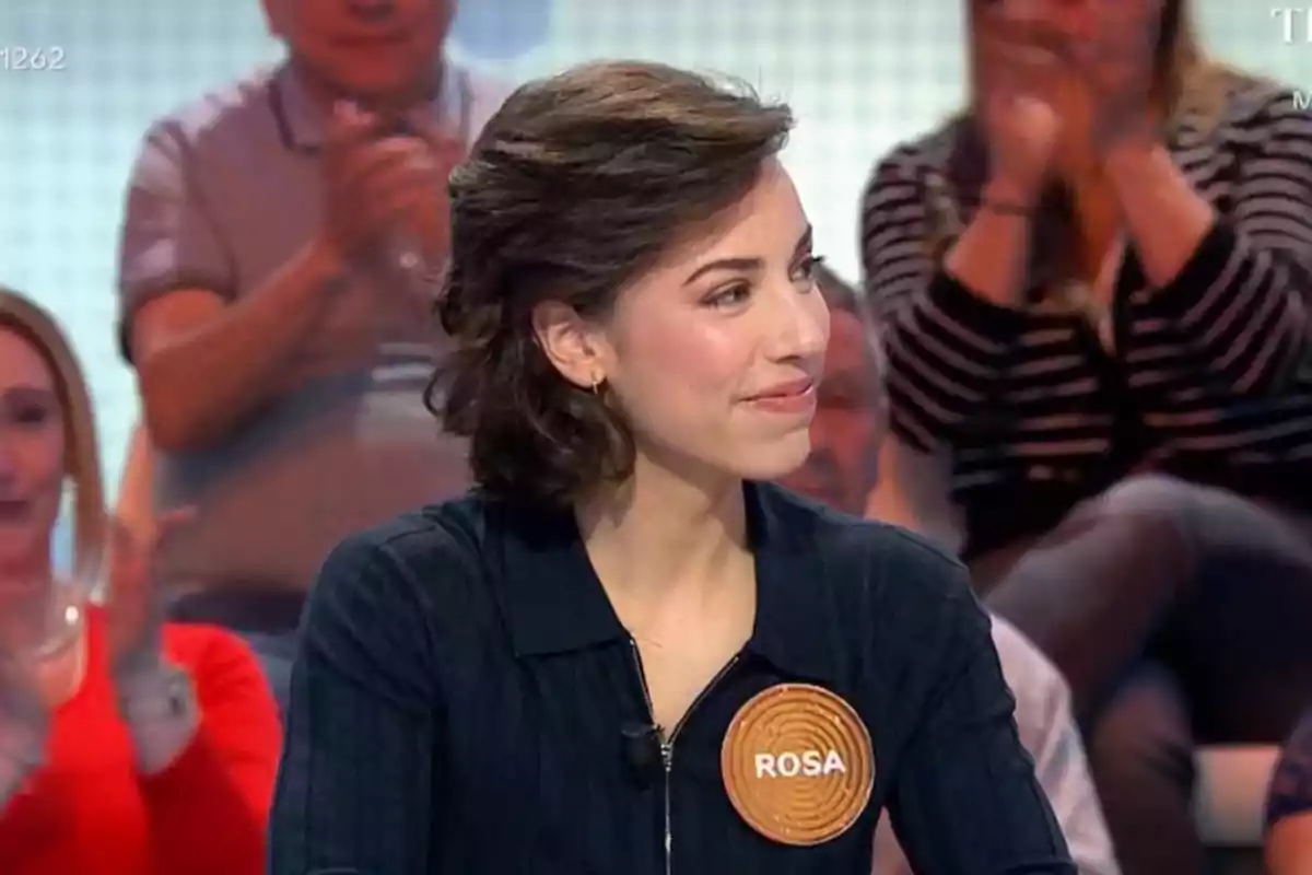 Rosa con cabello castaño y corto, vestida con una chaqueta oscura y un distintivo que dice Rosa con cabello castaño y corto, vestida con una chaqueta oscura y un distintivo que dice