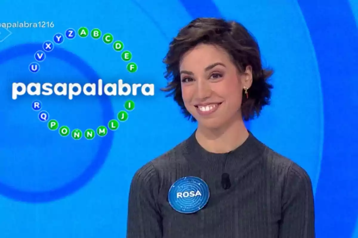 A smiling person on a television show with a blue background and a circle of letters around the "pasapalabra" logo.