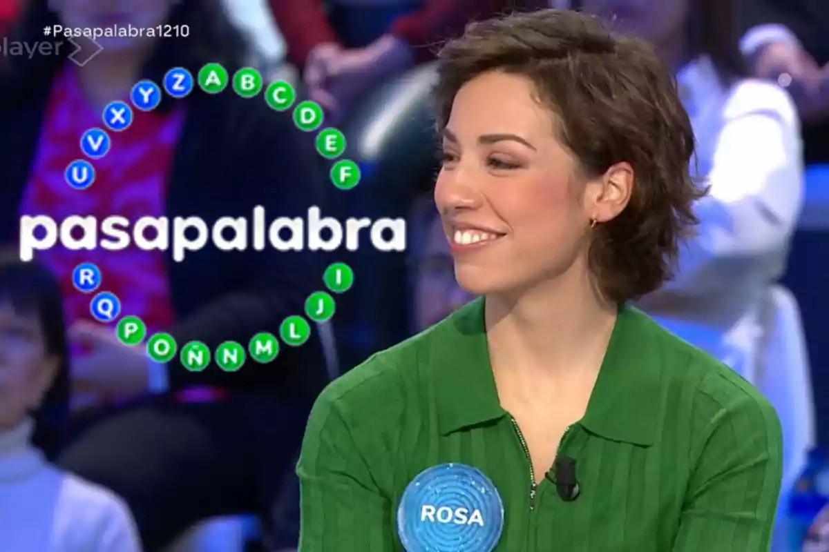 Rosa con camisa verde y una etiqueta que dice "ROSA" está en un programa de televisión llamado "Pasapalabra", con un círculo de letras en el fondo.