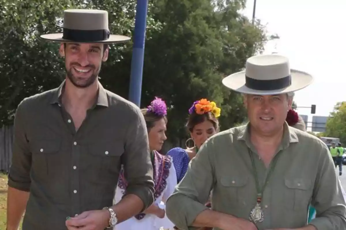 Sergio Rico y un hombre con sombrero cordobés y camisas verdes caminan al aire libre durante una festividad, acompañados por mujeres con flores en el cabello. Sergio Rico y un hombre con sombrero cordobés y camisas verdes caminan al aire libre durante una festividad, acompañados por mujeres con flores en el cabello.