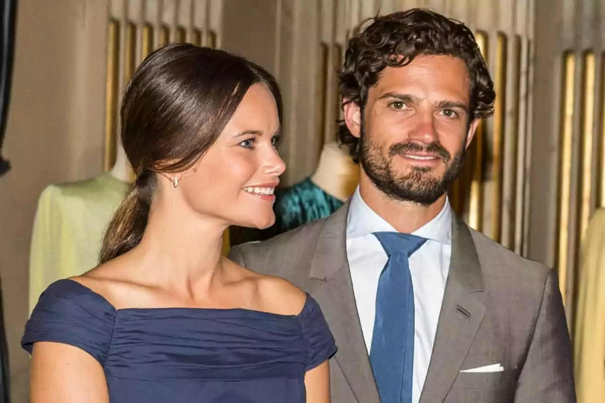 Una pareja elegantemente vestida sonríe mientras posa para una foto en un evento formal. Una pareja elegantemente vestida sonríe mientras posa para una foto en un evento formal.