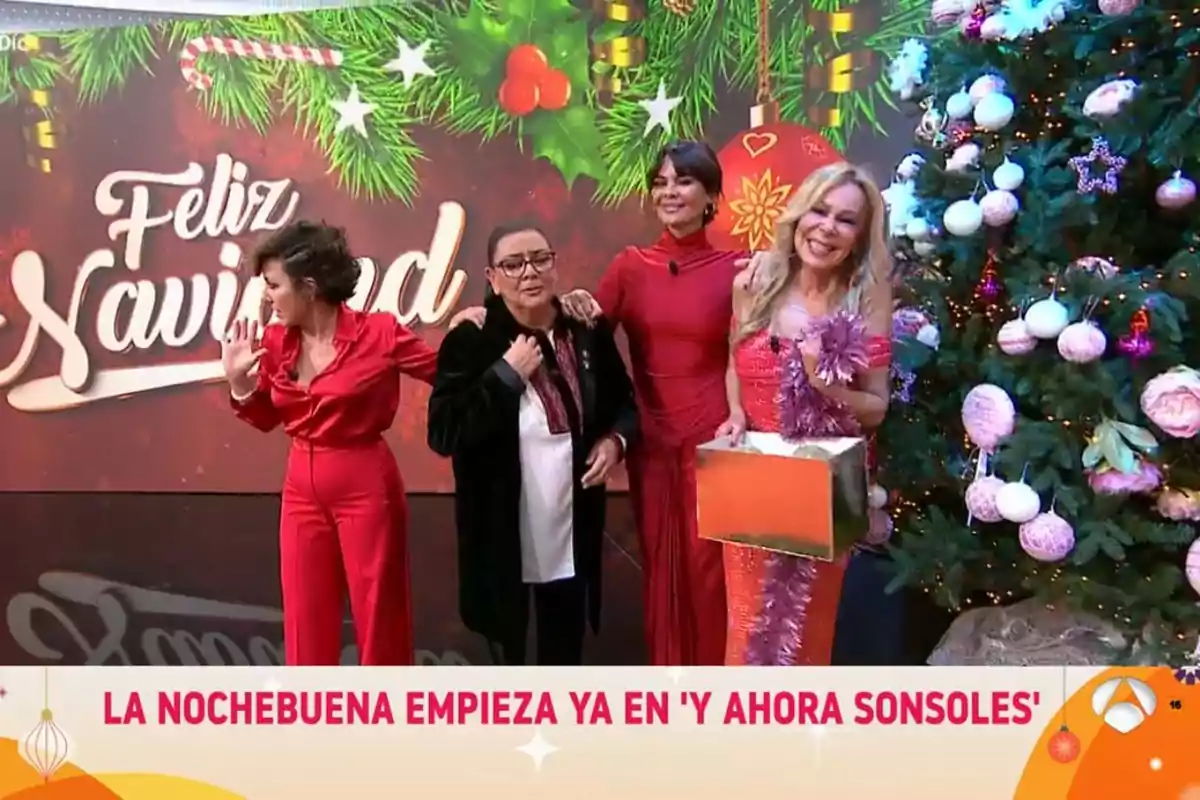 Un grupo de personas vestidas de rojo y negro posan sonrientes junto a un árbol de Navidad decorado, con un fondo que dice 