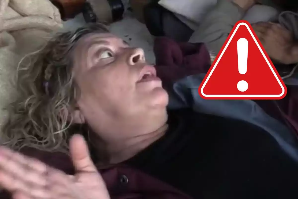 Terelu Campos acostada con expresión de sorpresa o preocupación y un icono de advertencia superpuesto.