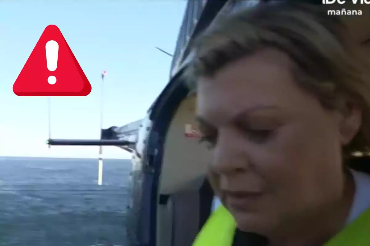 Terelu Campos con chaleco amarillo en un helicóptero sobre el mar con un ícono de advertencia en la esquina.