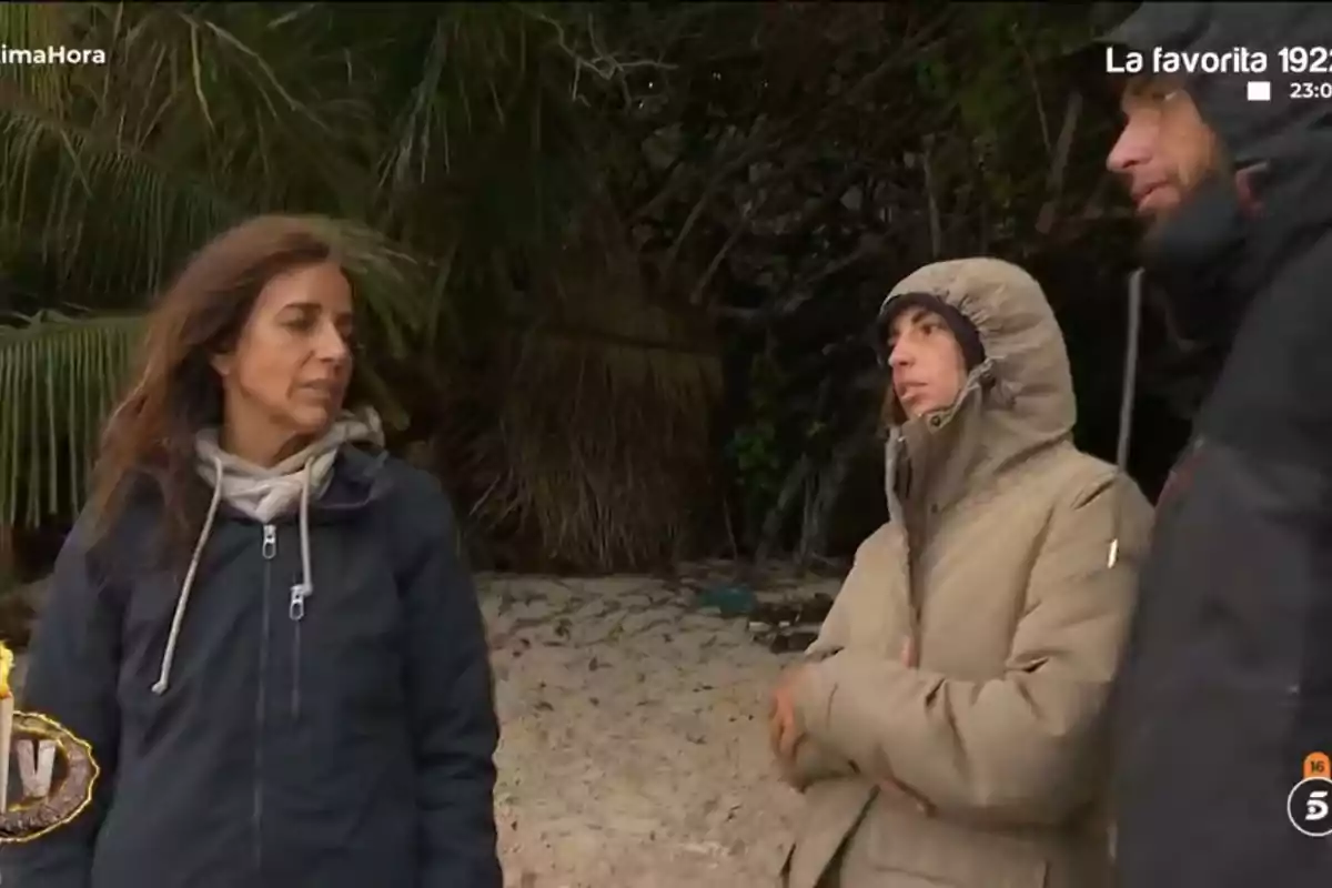 Carmen Alcayde, Montoya y Anita abrigados conversan en una playa con vegetación de fondo. Carmen Alcayde, Montoya y Anita abrigados conversan en una playa con vegetación de fondo.