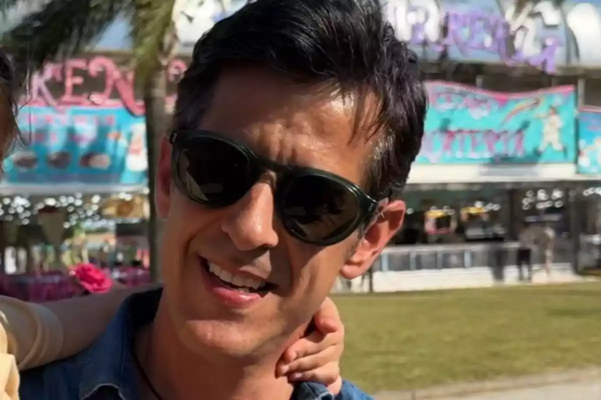 Víctor Janeiro con gafas de sol sonríe al aire libre con un fondo de feria colorido. Víctor Janeiro con gafas de sol sonríe al aire libre con un fondo de feria colorido.