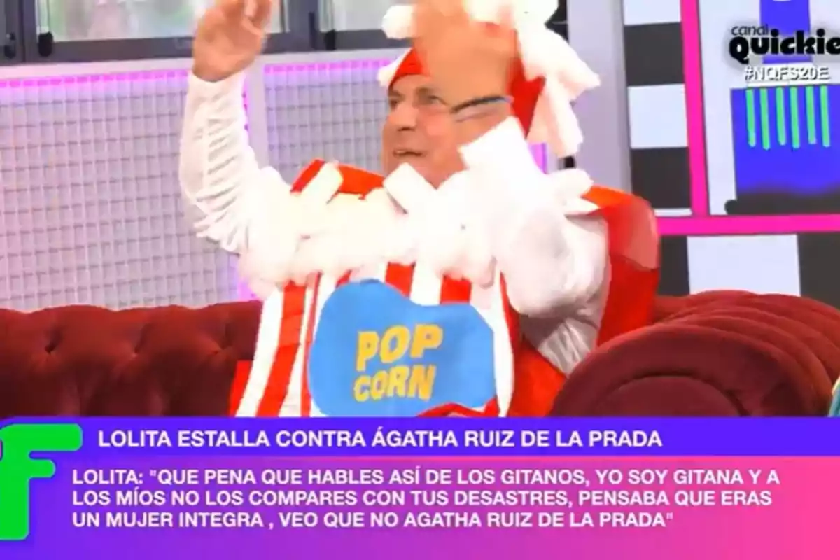 A person dressed as a popcorn box on a television show with text at the bottom mentioning an argument between Lolita and Ágatha Ruiz de la Prada. A person dressed as a popcorn box on a television show with text at the bottom mentioning an argument between Lolita and Ágatha Ruiz de la Prada.