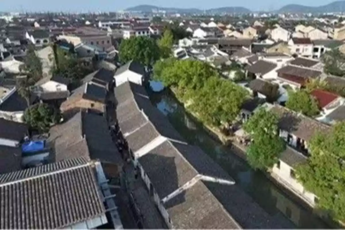 Vista aérea de un pueblo con techos tradicionales y un canal rodeado de árboles.