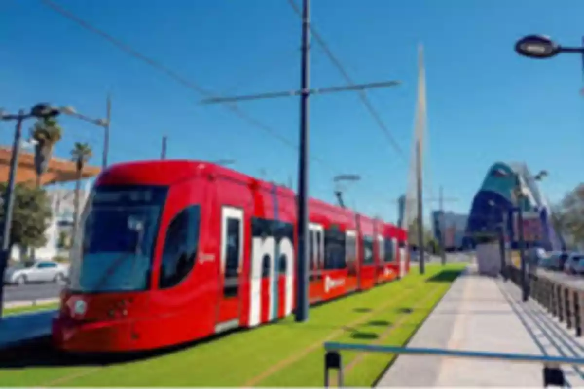 A red tram runs along a track in a modern city under a clear sky.