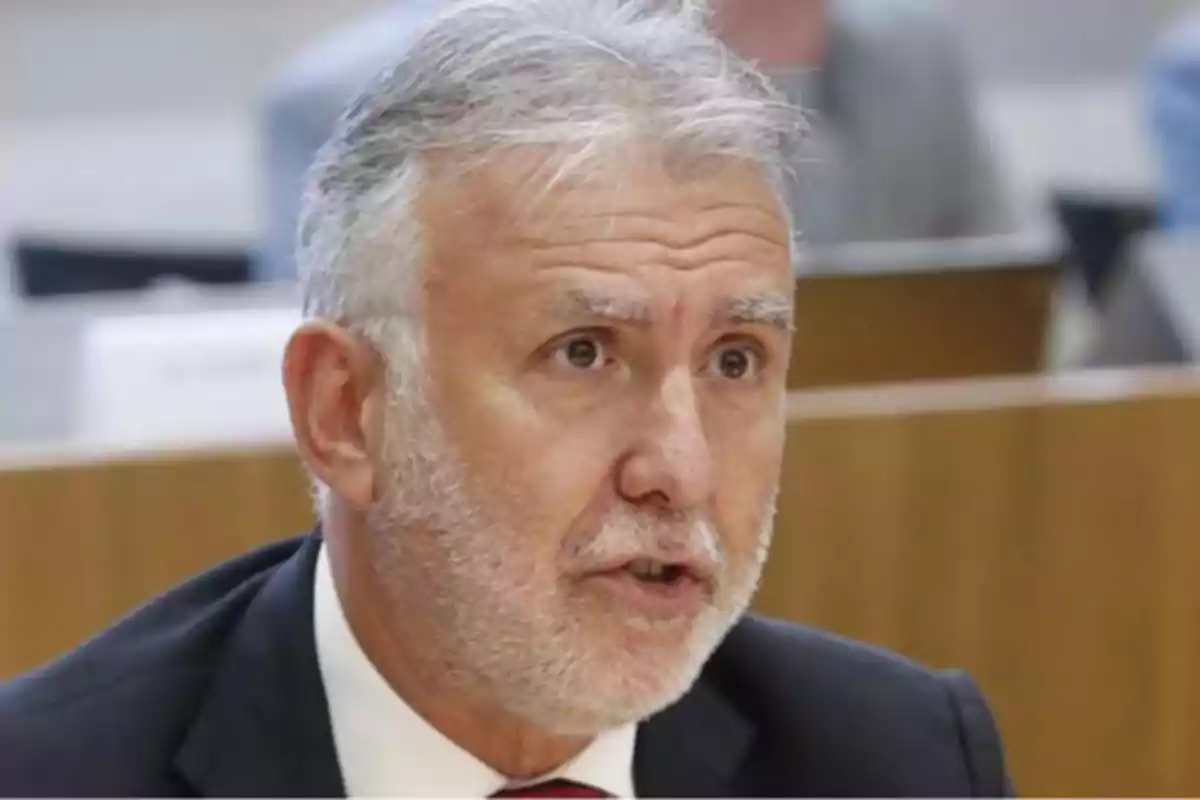 Un hombre de cabello canoso y barba hablando en un entorno formal.