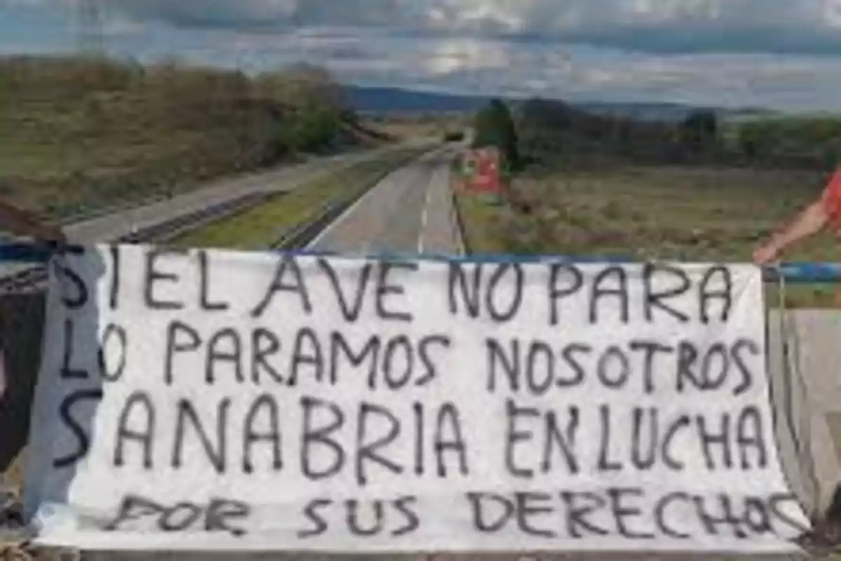 Pancarta de protesta colgada en un puente sobre una vía de tren en la que se lee un mensaje exigiendo que el tren AVE haga parada en Sanabria Pancarta de protesta colgada en un puente sobre una vía de tren en la que se lee un mensaje exigiendo que el tren AVE haga parada en Sanabria
