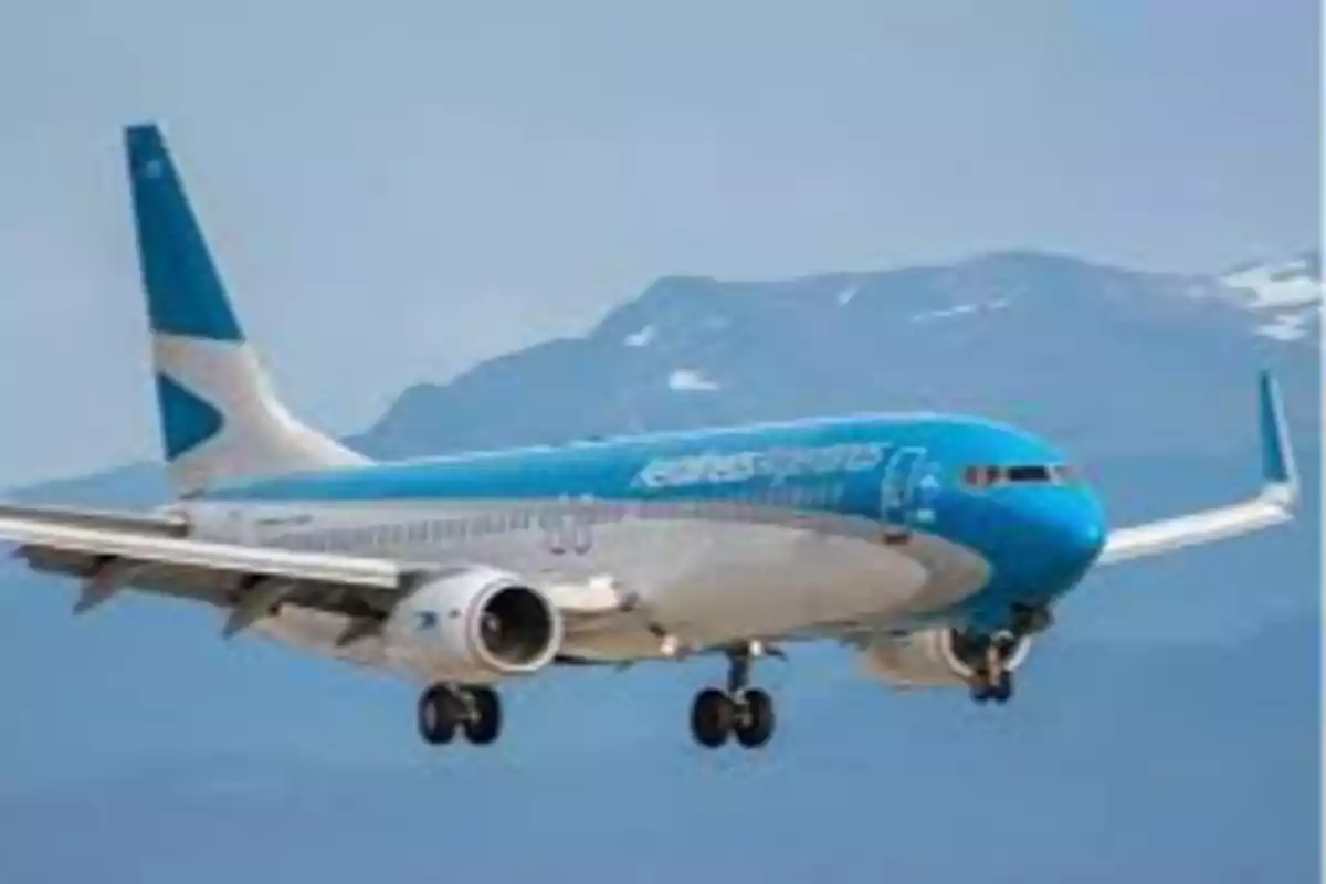 Avión de pasajeros azul y blanco en vuelo con montañas de fondo.