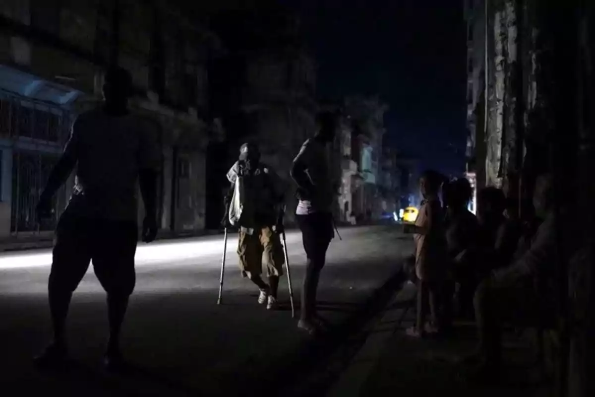 People walking and sitting on a dark street lit by dim lights in an urban setting.