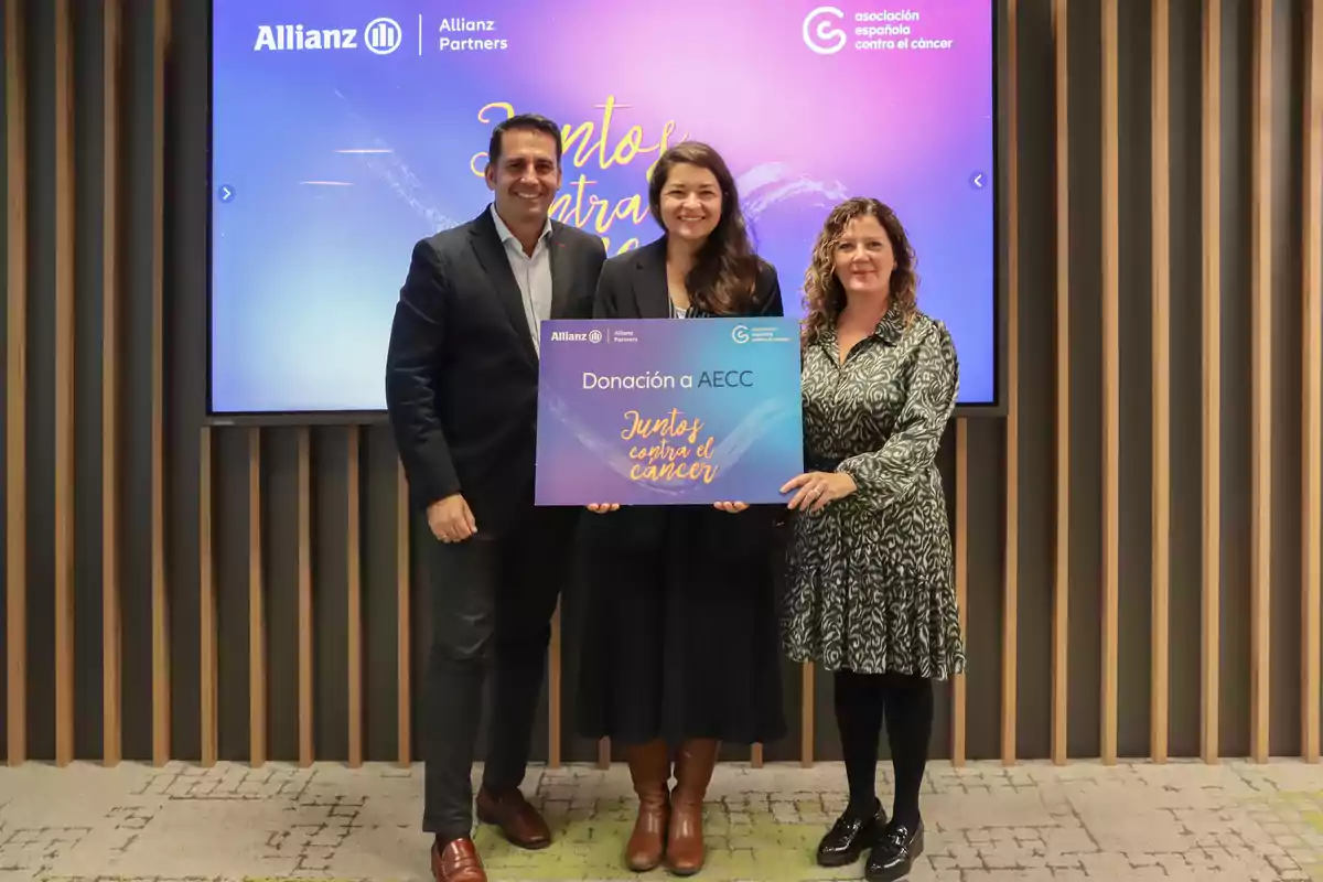 Tres personas posan con un cartel de donación a la Asociación Española Contra el Cáncer en un evento de Allianz Partners.