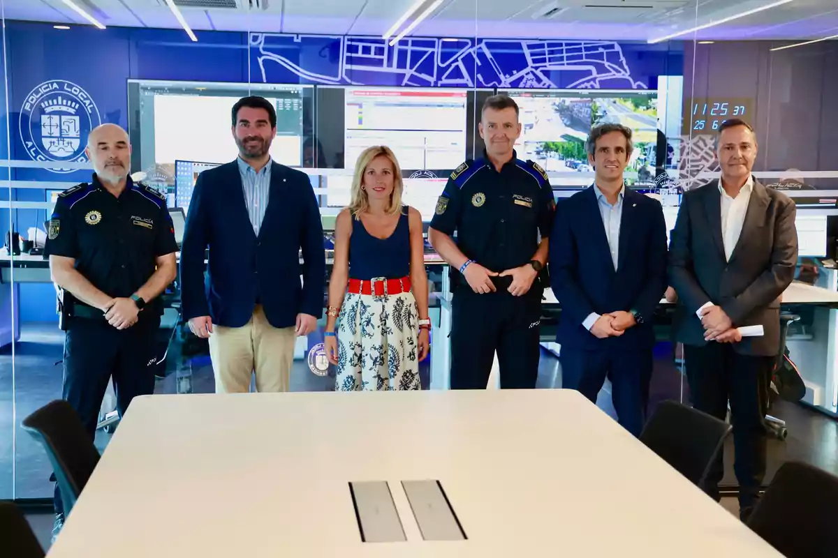 Un grupo de personas, incluyendo oficiales de policía y civiles, posan para una foto en una sala de control con pantallas y mapas en el fondo.