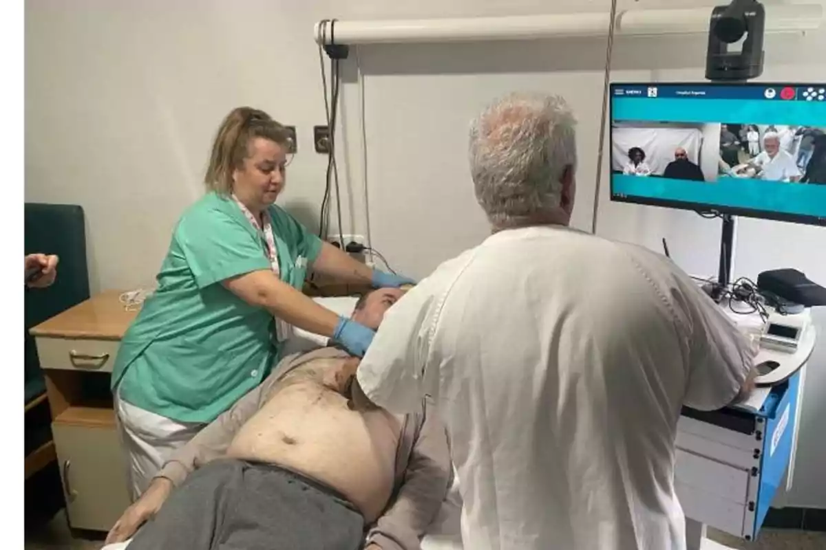 Personal médico atendiendo a un paciente acostado en una camilla mientras observan una pantalla con una videollamada.