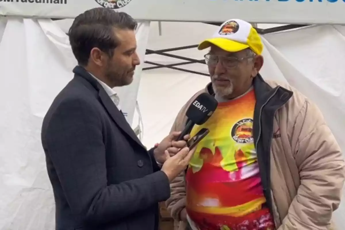 Un reportero entrevista a un hombre mayor que lleva una gorra y una camiseta colorida.