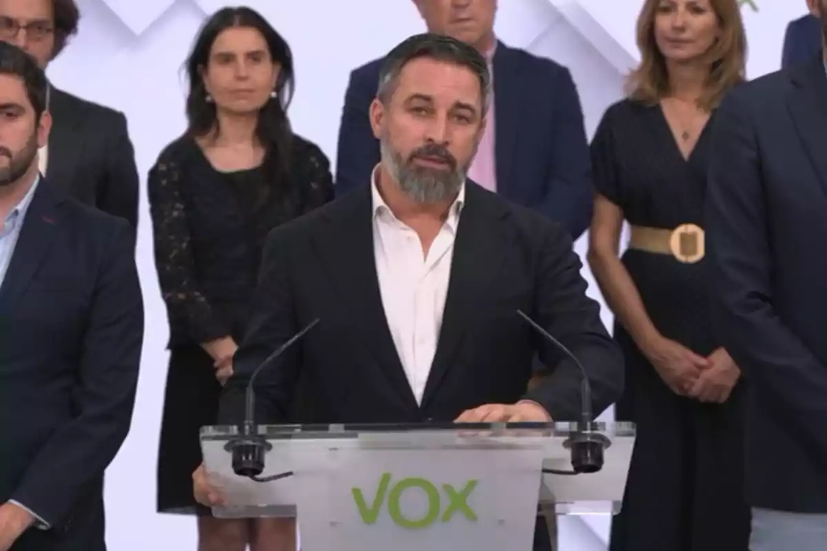 Un grupo de personas, con un hombre en primer plano hablando en un podio con el logotipo de VOX.