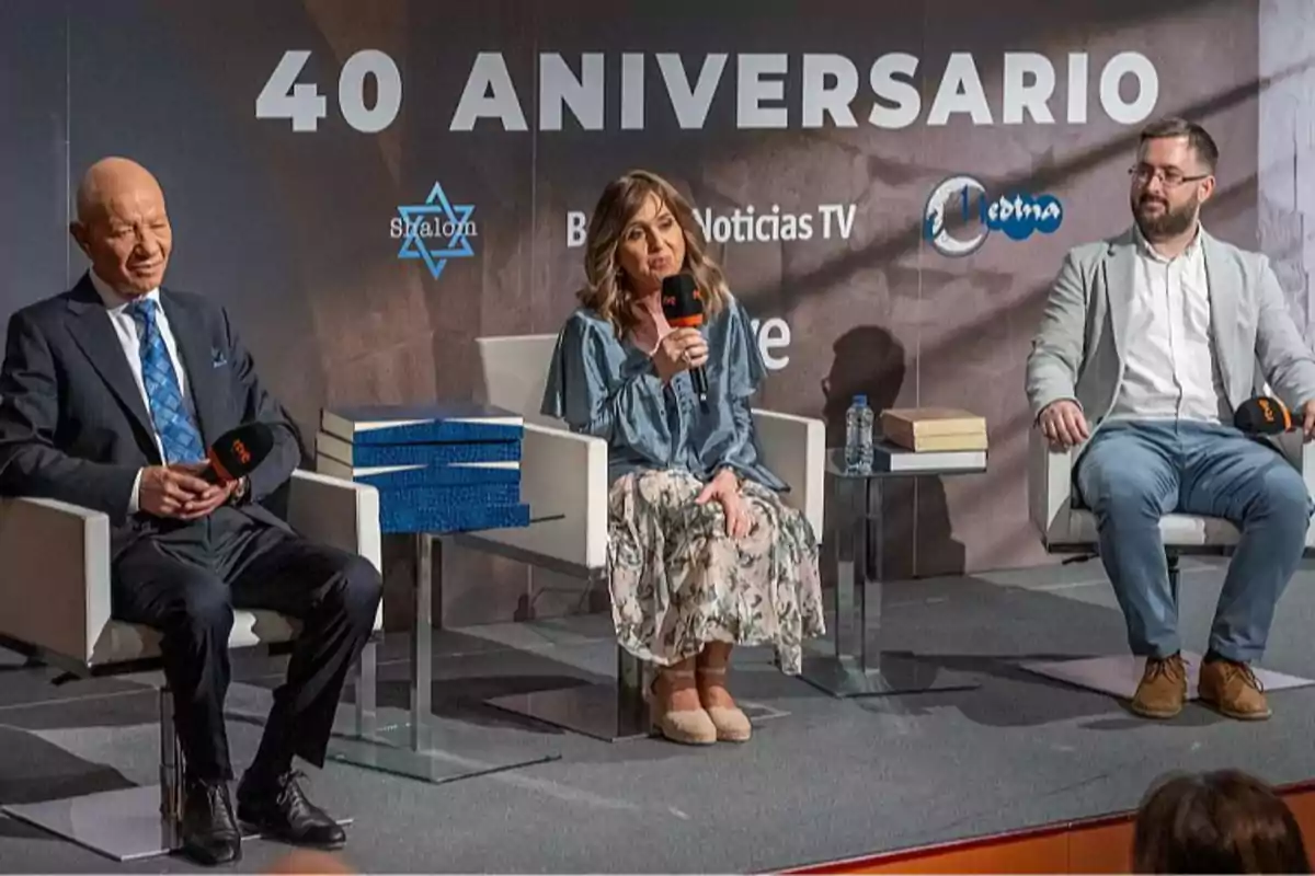 Tres personas sentadas en sillones participan en un evento con motivo del 40 aniversario de un programa, sosteniendo micrófonos y conversando en un escenario con fondo decorado y logotipos.