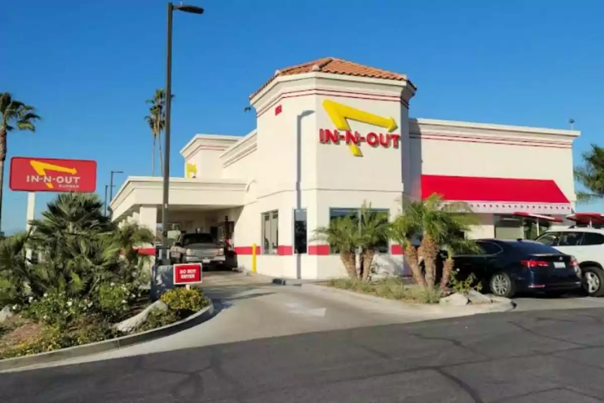 A fast-food restaurant with a red and yellow sign surrounded by palm trees and parked cars. A fast-food restaurant with a red and yellow sign surrounded by palm trees and parked cars.