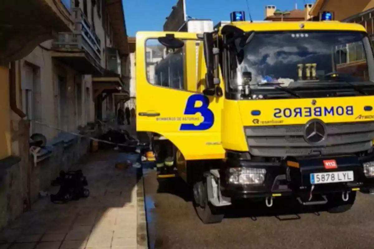 Camión de bomberos amarillo de Asturias estacionado frente a un edificio residencial con la puerta abierta y equipo de emergencia en la acera Camión de bomberos amarillo de Asturias estacionado frente a un edificio residencial con la puerta abierta y equipo de emergencia en la acera