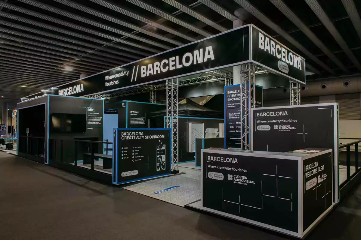 Un stand de exhibición con el tema de Barcelona, destacando la creatividad y el talento, con estructuras metálicas y paneles informativos iluminados.