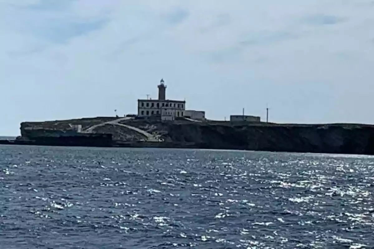 Faro en una isla rocosa visto desde el mar con cielo parcialmente nublado.