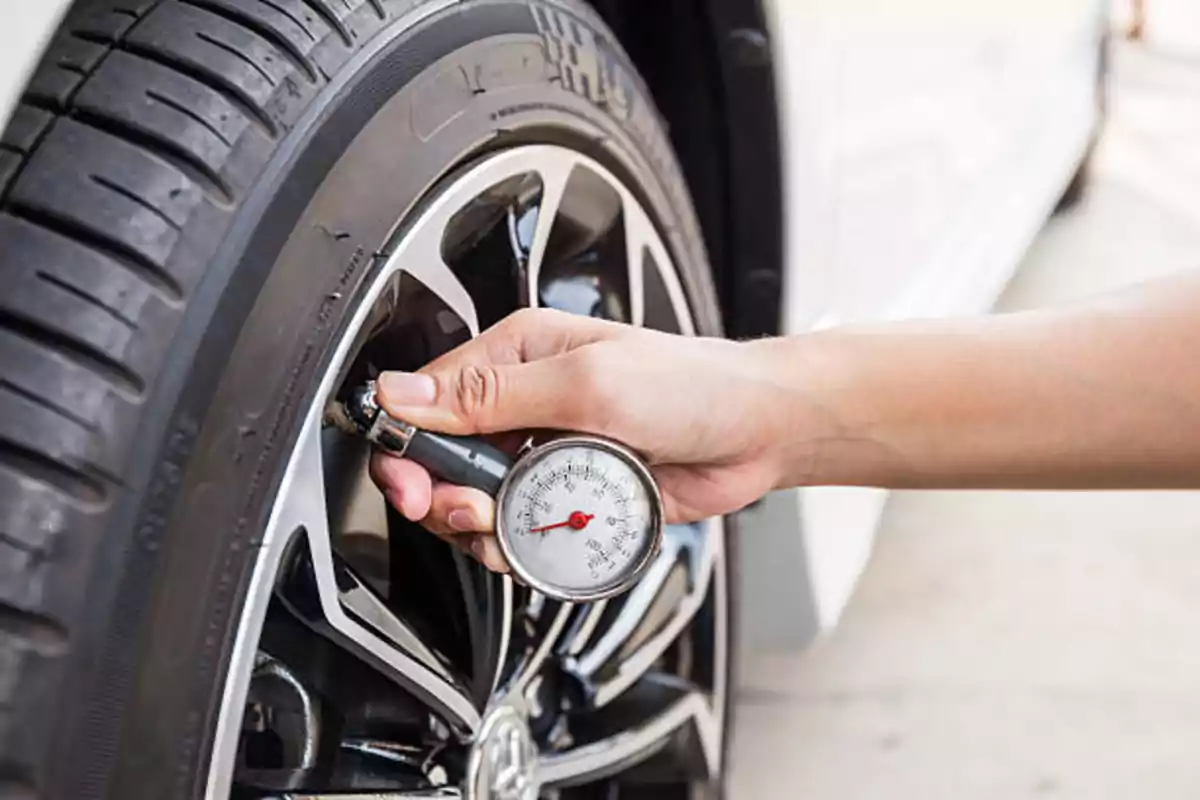 Persona midiendo la presión de aire de una llanta de automóvil con un manómetro.