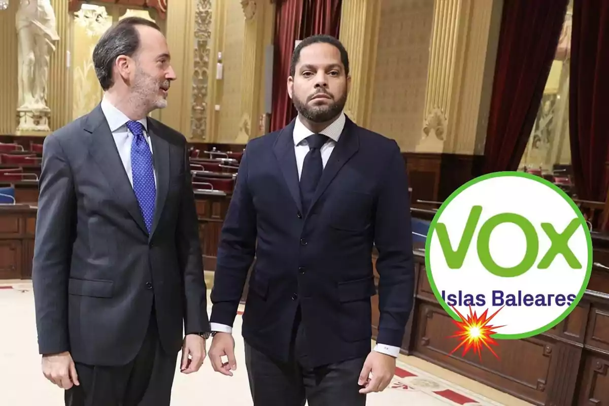 Dos hombres de pie en una sala con decoración clásica, uno de ellos con traje gris y corbata azul, el otro con traje oscuro y corbata negra, junto a un logotipo de VOX Islas Baleares.