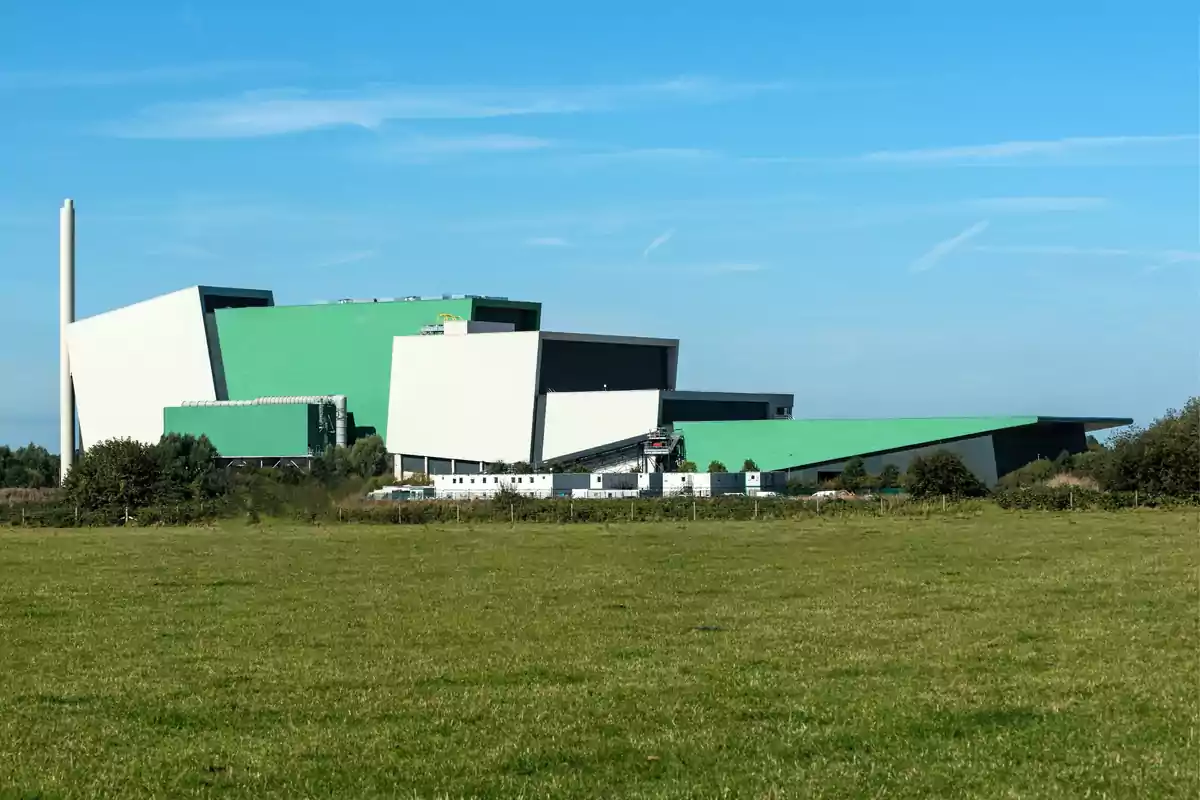 Edificio industrial moderno con techos verdes y paredes blancas en un campo verde bajo un cielo azul claro.