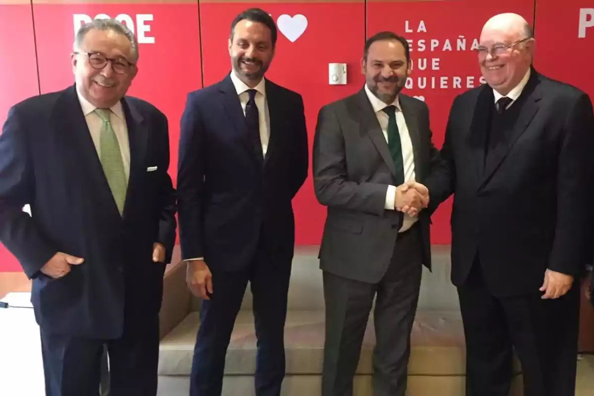 Cuatro hombres de traje posan frente a un fondo rojo con el logotipo del PSOE.