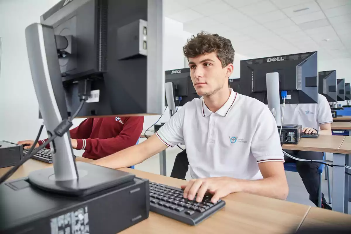 Un joven concentrado trabajando en una computadora en un aula de informática.