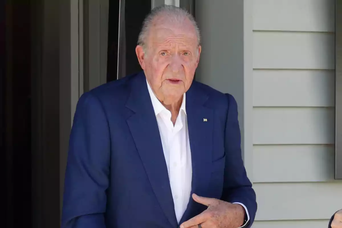 Juan Carlos I con traje azul y camisa blanca está de pie frente a una puerta. Juan Carlos I con traje azul y camisa blanca está de pie frente a una puerta.
