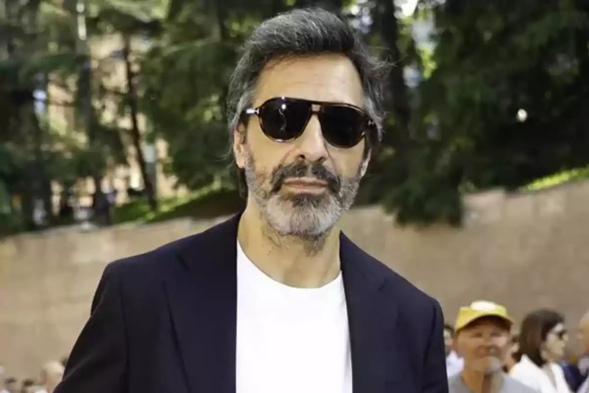 Juan del Val, vestido con una camiseta blanca y chaqueta oscura, en un entorno al aire libre con árboles de fondo. Juan del Val, vestido con una camiseta blanca y chaqueta oscura, en un entorno al aire libre con árboles de fondo.