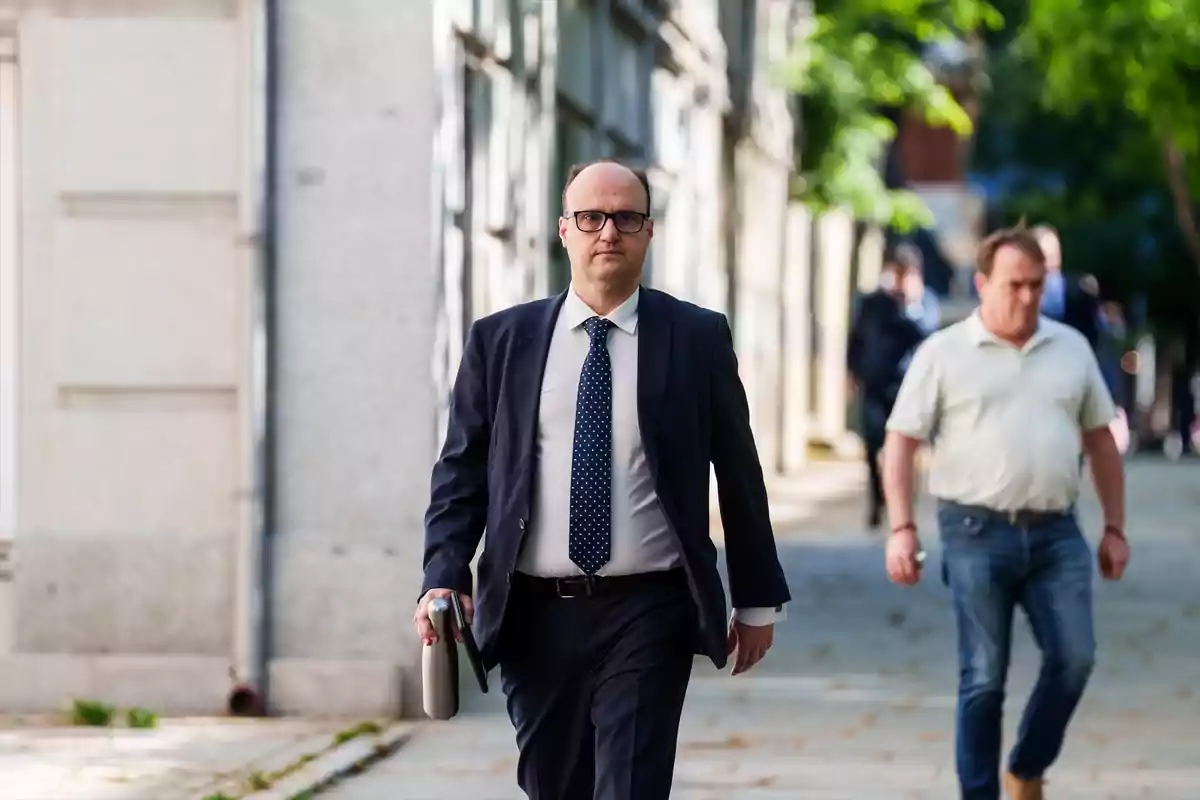 Un hombre con traje y corbata camina por una acera llevando un portafolio en la mano. Un hombre con traje y corbata camina por una acera llevando un portafolio en la mano.