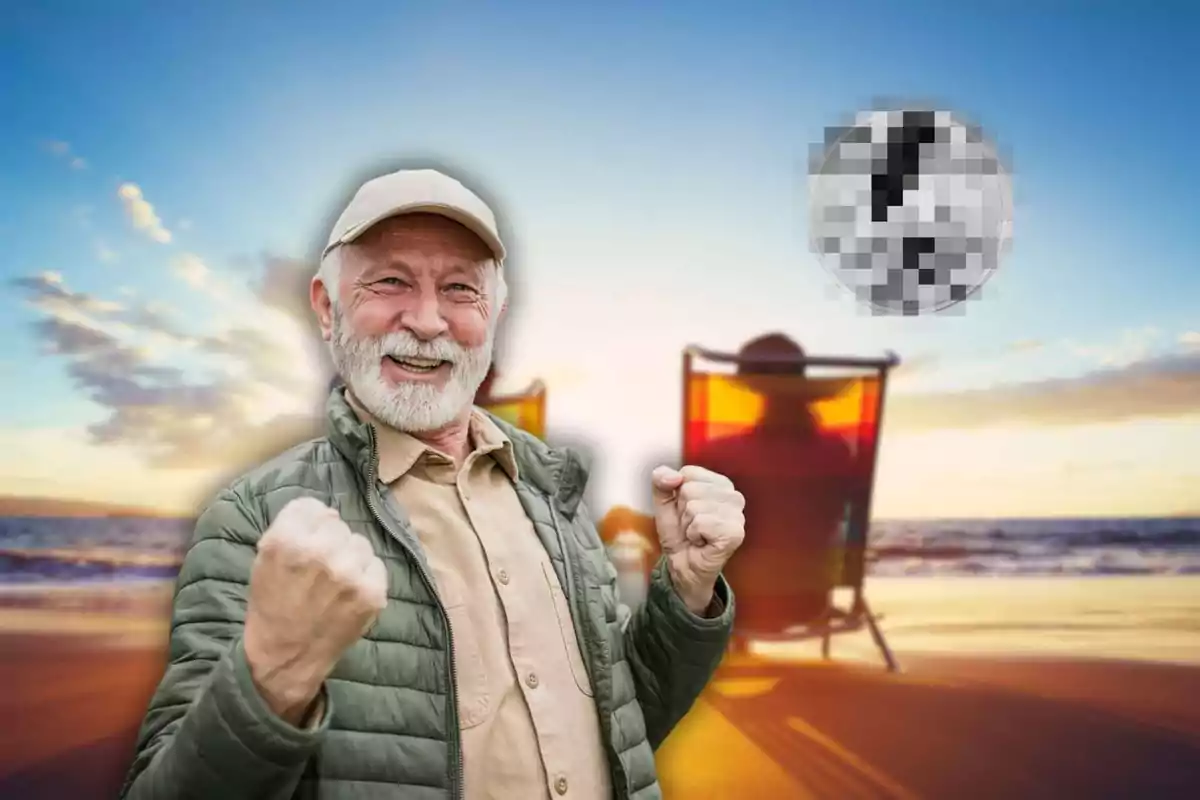 Hombre mayor sonriente con gorra y chaqueta verde levantando los puños en señal de victoria en una playa al atardecer con dos personas sentadas en sillas de playa al fondo.