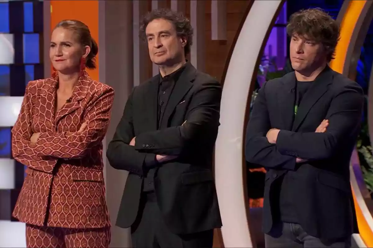 Samantha Vallejo-Nágera, Pepe Rodríguez y Jordi Cruz de pie con los brazos cruzados, vestidas de manera formal, en un entorno iluminado y colorido en MasterChef. Samantha Vallejo-Nágera, Pepe Rodríguez y Jordi Cruz de pie con los brazos cruzados, vestidas de manera formal, en un entorno iluminado y colorido en MasterChef.