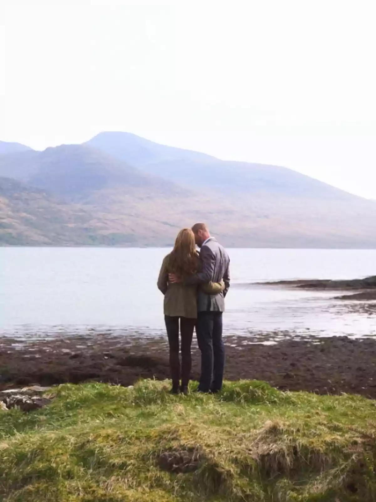 A couple embraced from behind looking at a lake with mountains in the background. A couple embraced from behind looking at a lake with mountains in the background.