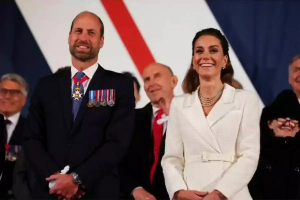 A man and a woman smile while standing at a formal event surrounded by other people. A man and a woman smile while standing at a formal event surrounded by other people.