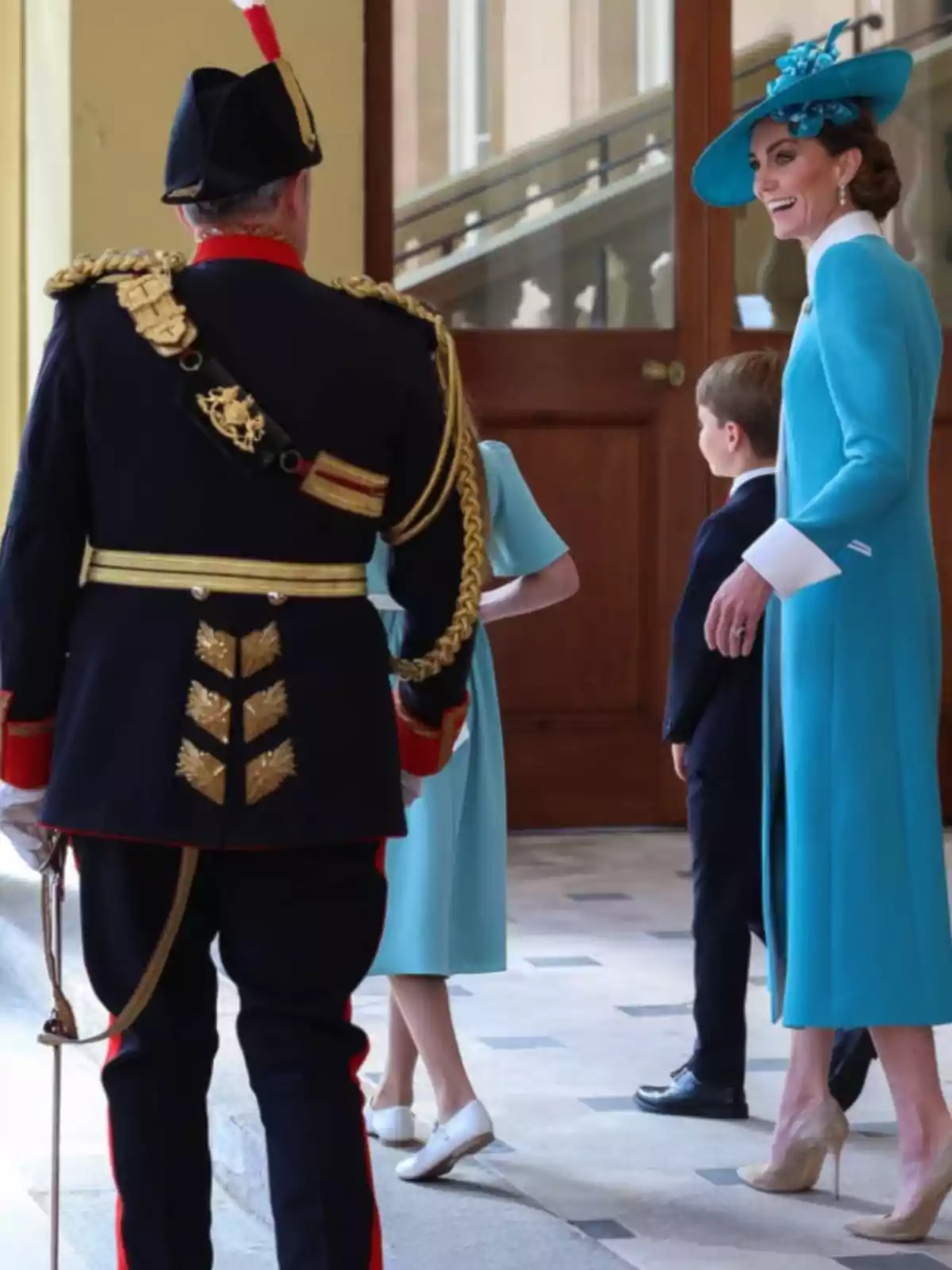 An elegantly dressed woman in blue with a matching hat smiles as she talks with a man in a formal uniform and two children in an official-looking building. An elegantly dressed woman in blue with a matching hat smiles as she talks with a man in a formal uniform and two children in an official-looking building.