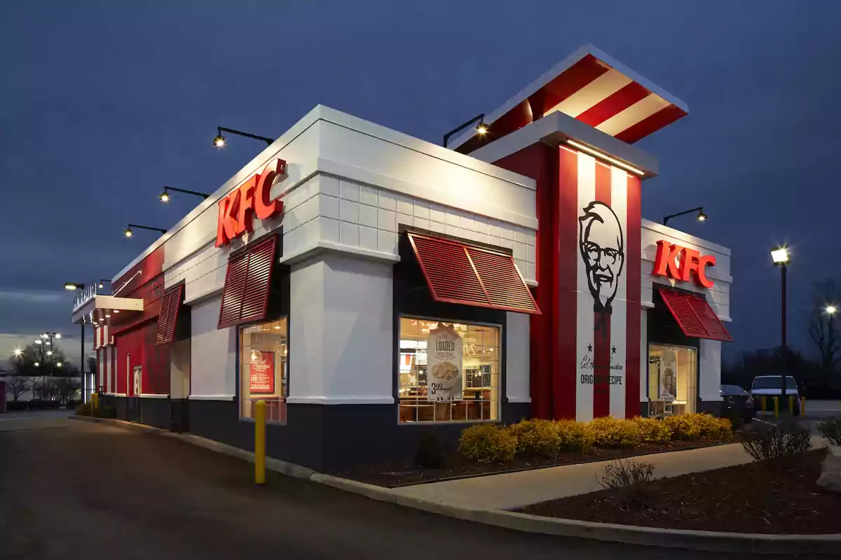 Un restaurante de comida rápida KFC iluminado por la noche con el logotipo visible en la fachada. Un restaurante de comida rápida KFC iluminado por la noche con el logotipo visible en la fachada.
