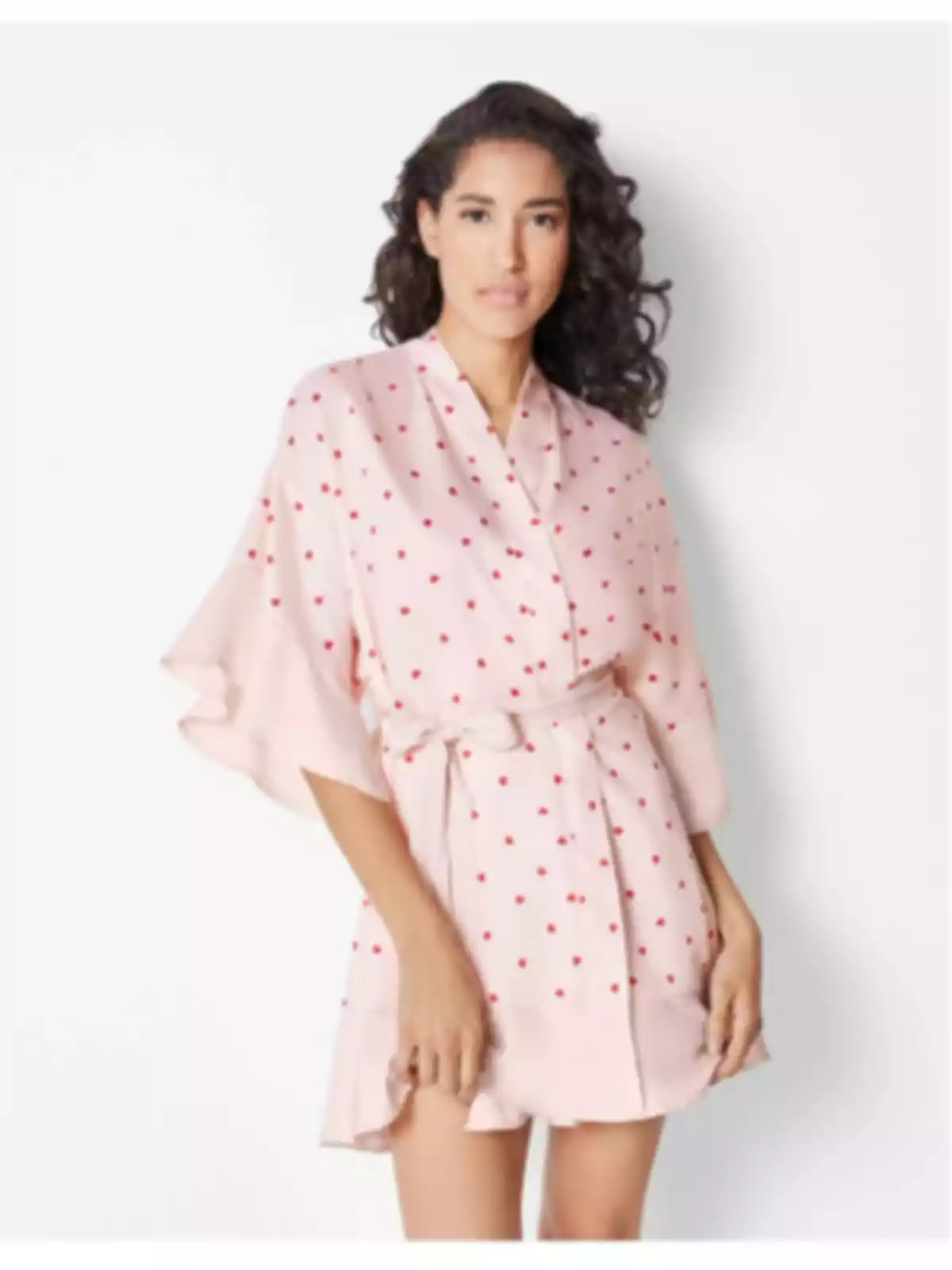 Mujer con cabello rizado usando un vestido corto rosa claro con estampado de pequeños puntos rojos y cinturón del mismo tejido Mujer con cabello rizado usando un vestido corto rosa claro con estampado de pequeños puntos rojos y cinturón del mismo tejido