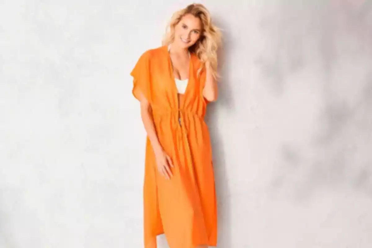 Mujer rubia sonriente usando un vestido naranja suelto y fondo claro difuminado Mujer rubia sonriente usando un vestido naranja suelto y fondo claro difuminado