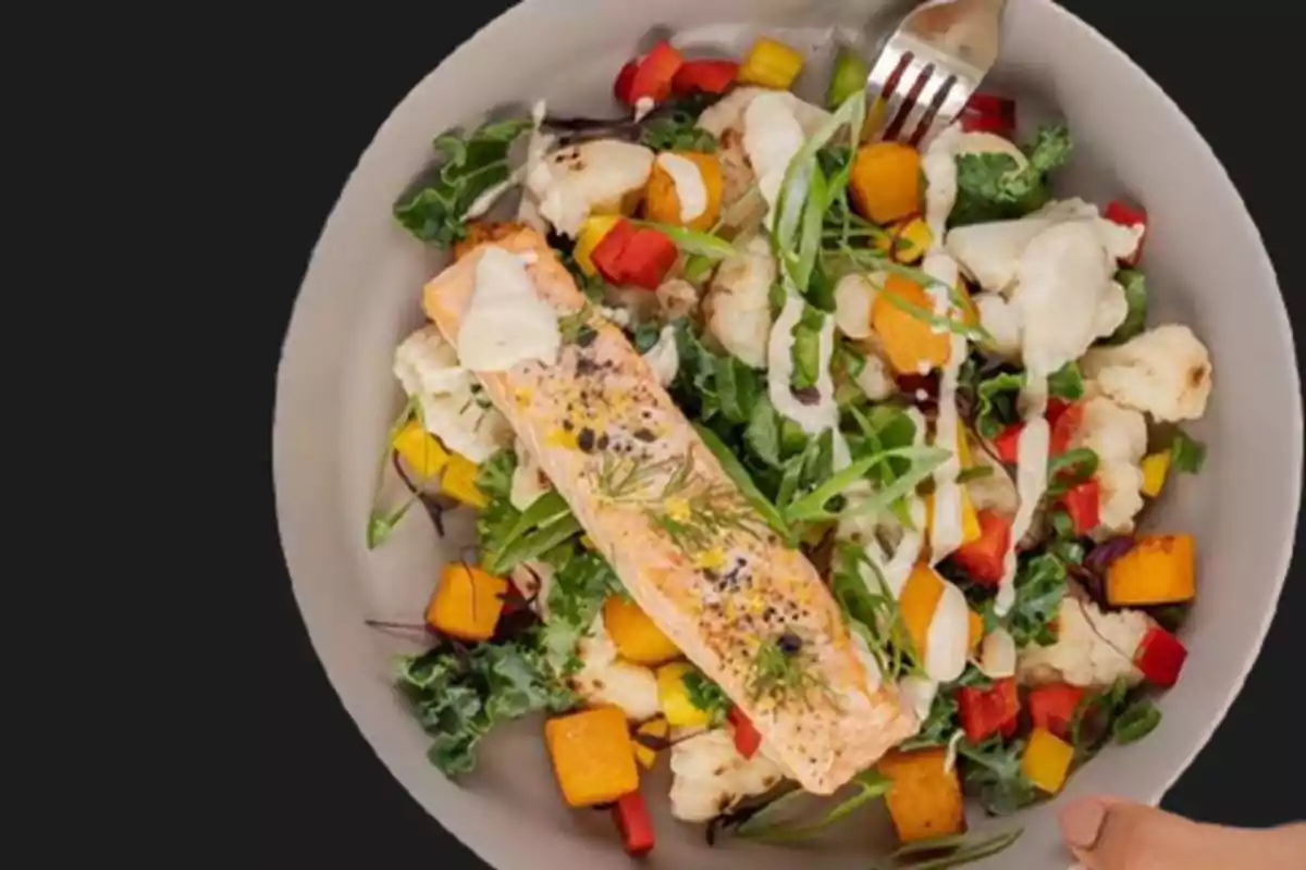 Plato de ensalada con salmón, verduras mixtas y aderezo, acompañado de un tenedor.