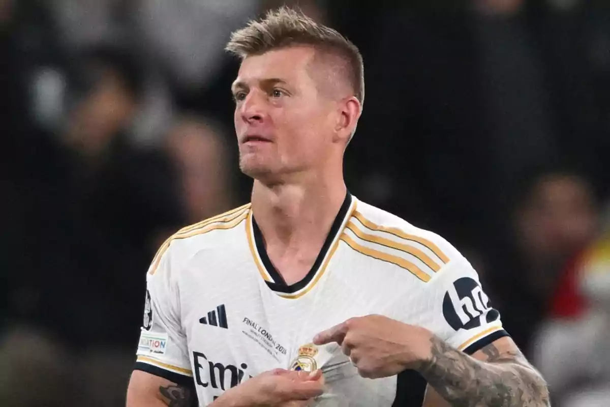 Un jugador de fútbol con la camiseta del Real Madrid señalando el escudo del equipo.