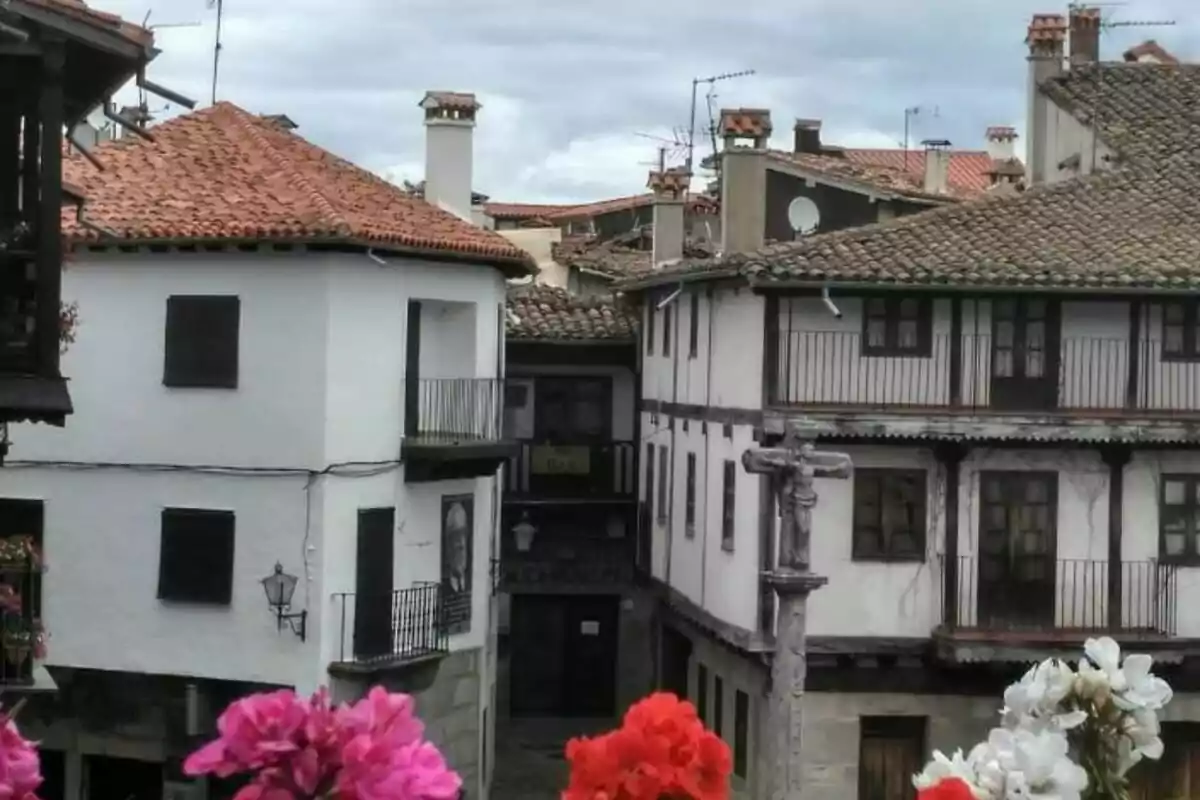 Una calle estrecha con casas de estilo tradicional, balcones de madera y techos de tejas rojas, con flores coloridas en primer plano.