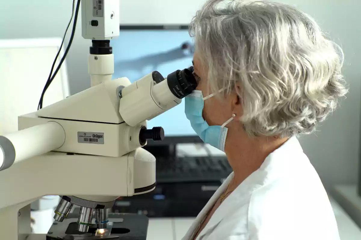 Person wearing a mask looking through a microscope in a laboratory.