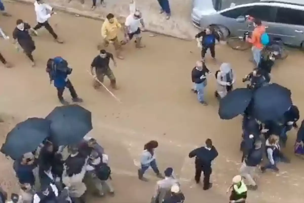 Un grupo de personas camina por un camino de tierra, algunas llevan paraguas negros y otras están equipadas con cámaras y mochilas, mientras un vehículo y una bicicleta se encuentran estacionados al lado del camino. Un grupo de personas camina por un camino de tierra, algunas llevan paraguas negros y otras están equipadas con cámaras y mochilas, mientras un vehículo y una bicicleta se encuentran estacionados al lado del camino.
